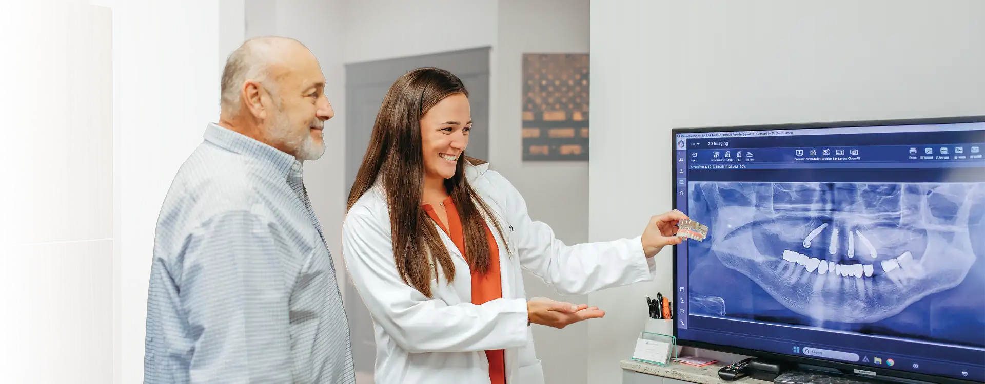 Image of Dr. Leigh Haynes showing a patient a computer monitor displaying an X-ray of dental implants.